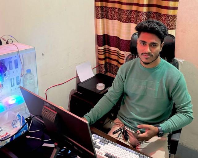 Alvi Hassan seated at his desk with a monitor, keyboard and computer hardware beside him